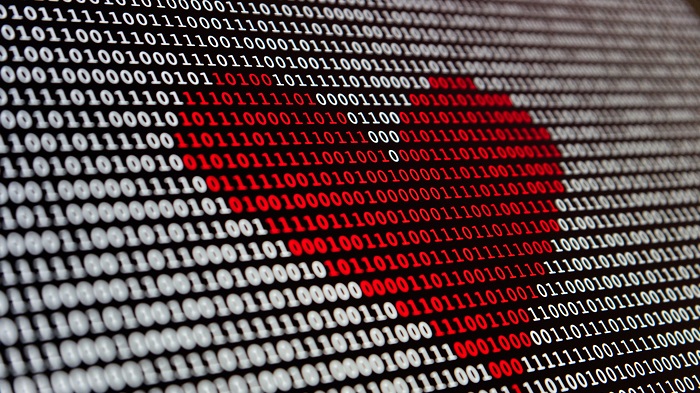Imagem de uma tela exibindo uma sequência de números binários (0s e 1s), dispostos em linhas horizontais. No centro da imagem, um coração é formado por números binários vermelhos, contrastando com o fundo composto por números binários brancos. A composição cria a figura de um coração no meio de uma massa de dados. O padrão binário é contínuo e preenche toda a tela, com a forma do coração destacando-se claramente no meio.