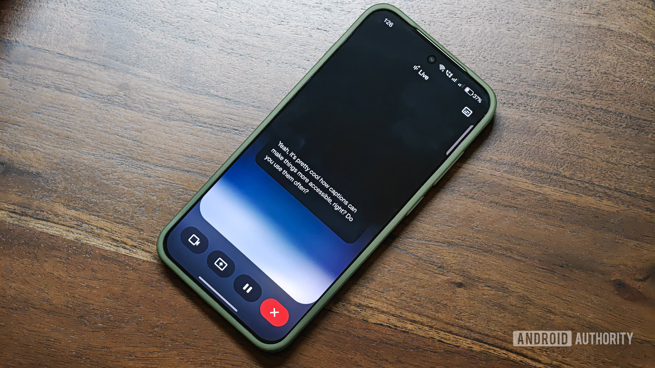 Legendas ao vivo do Google Gemini no aplicativo Android rodando em um OnePlus 13s mantido sobre a superf&iacute;cie de uma mesa de madeira.
