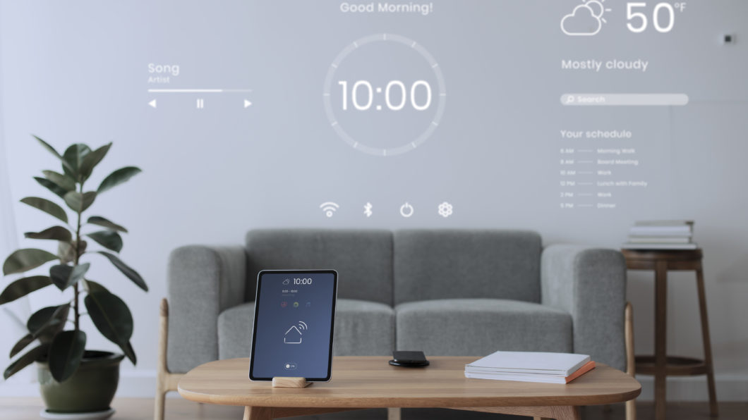 Imagem ilustra uma casa inteligente, com um tablet à frente e um relógio ao centro.