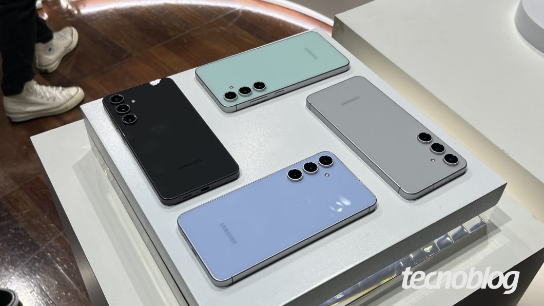 Quatro aparelhos Galaxy S24 FE, nas cores preto, cinza, azul e verde, lado a lado em uma mesa, com a parte de trás para cima