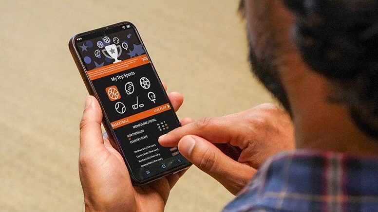 Foto de smartphone na mão de homem usando um aplicativo de apostas (bets)