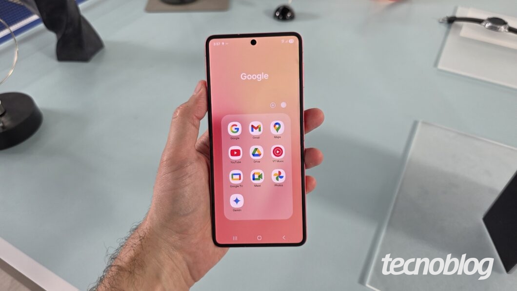 Mão segurando smartphone, visto de frente, exibindo a pasta de aplicativos do Google