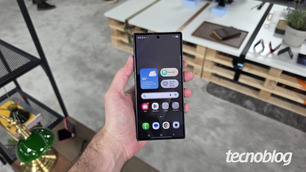 M&atilde;o segurando smartphone dobr&aacute;vel fechado, exibindo a tela inicial da One UI