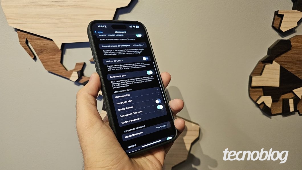 M&atilde;o segurando um iPhone na tela de configura&ccedil;&otilde;es de mensagens, que possui uma fun&ccedil;&atilde;o para ativar a tecnologia RCS
