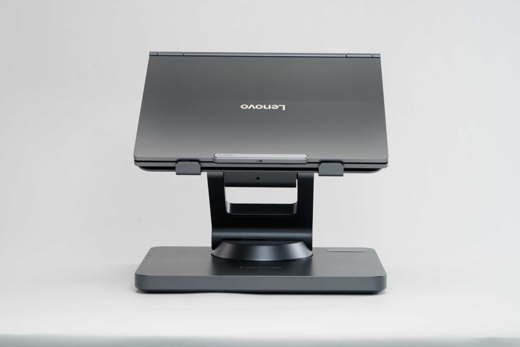 Imagem mostra um suporte de notebook da marca Lonovo, na cor cinza escovado, com um notebook da fabricante. O fundo da imagem &eacute; branco.