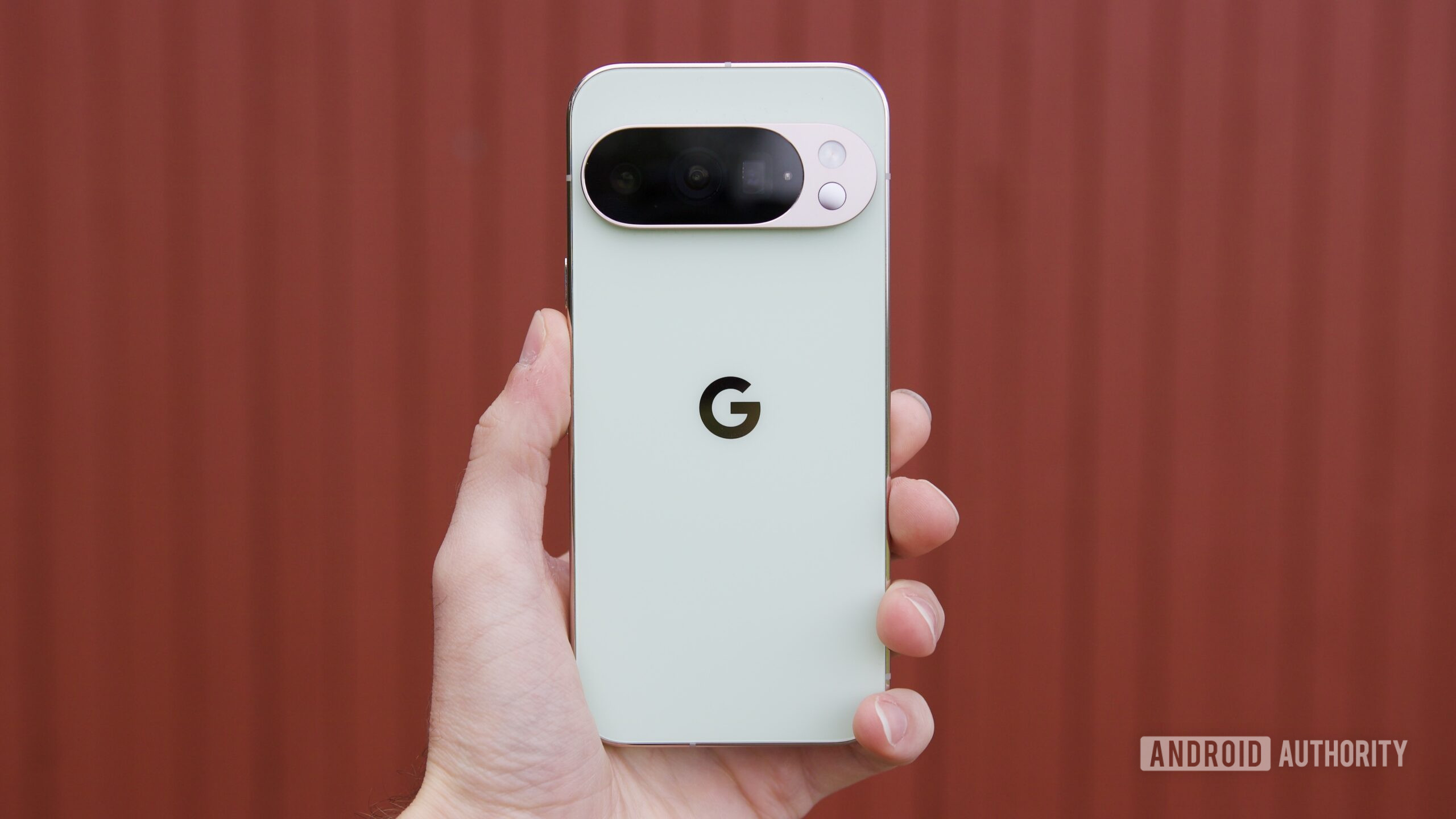 Google Pixel 10 Pro Jade de volta 10 Alguém segurando o Google Pixel 10 Pro contra um fundo vermelho.