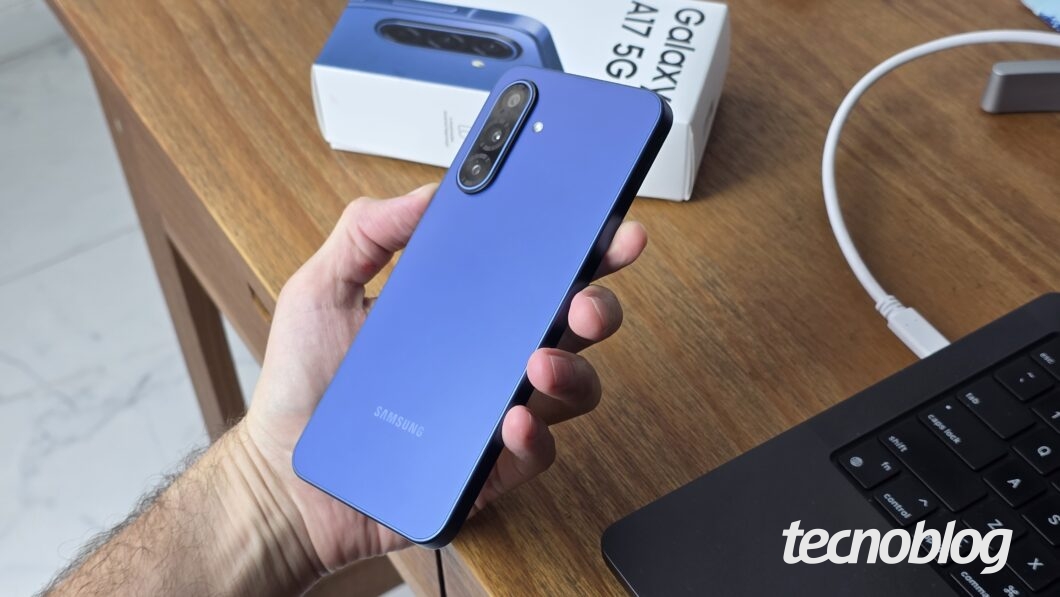 Mão segurando smartphone na tela de boas vindas, sobre uma mesa que também tem uma caixa e um notebook