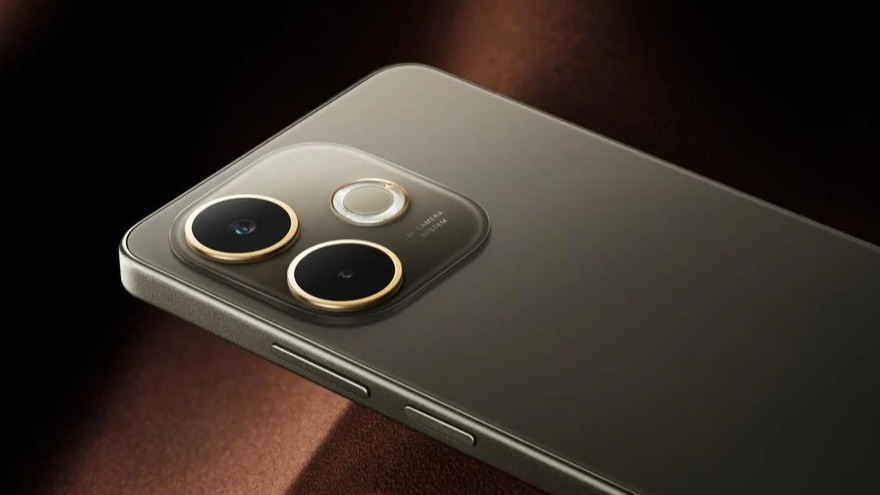 Imagem mostra um smartphone Oppo A5 Pro 5G com a parte traseira em tom marrom escuro, com um leve brilho reflexivo no centro. O módulo de câmera, localizado no canto superior esquerdo, possui duas lentes redondas de bordas douradas, um flash e uma pequena lente auxiliar, tudo em um formato que se sobressai ligeiramente da superfície do aparelho. Ao lado, uma pequena inscrição de "AI Camera" é visível. Os botões de volume e energia estão na lateral direita. O fundo da imagem é marrom.