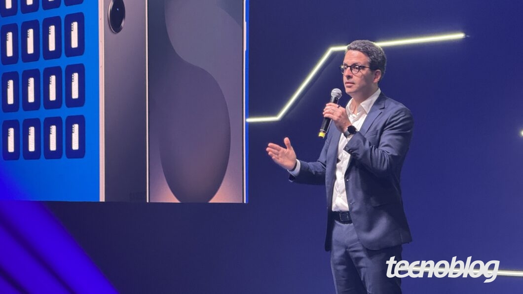 Homem de pé discursa com microfone na mão