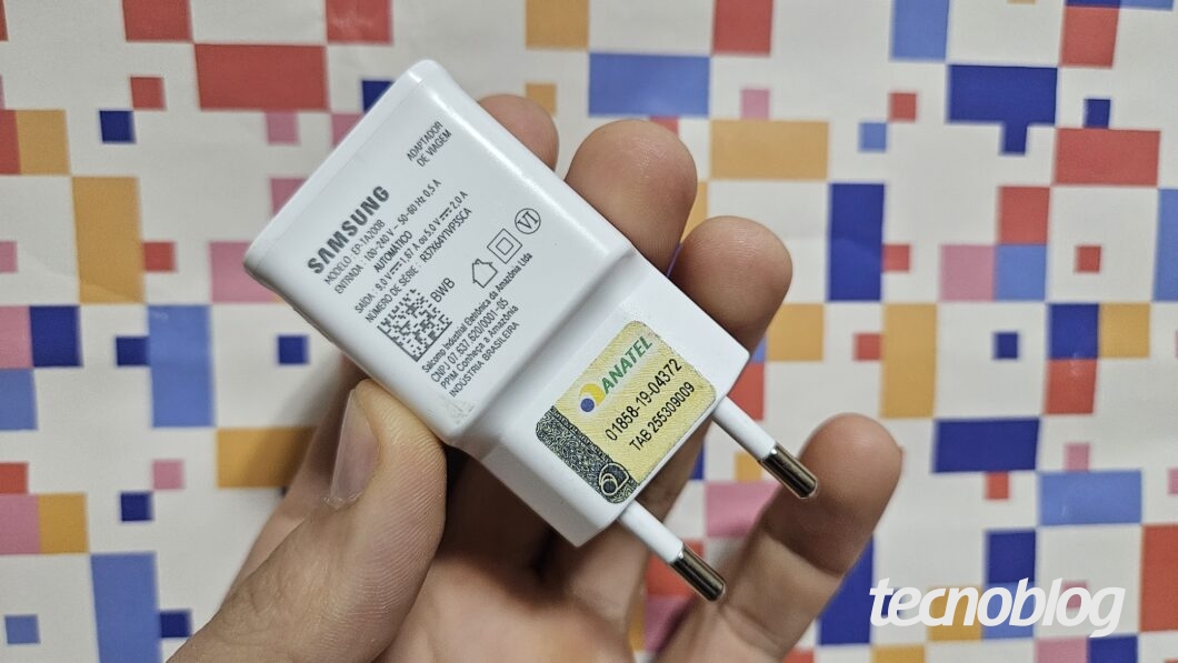 M&atilde;o segurando carregador de celular sobre fundo abstrato