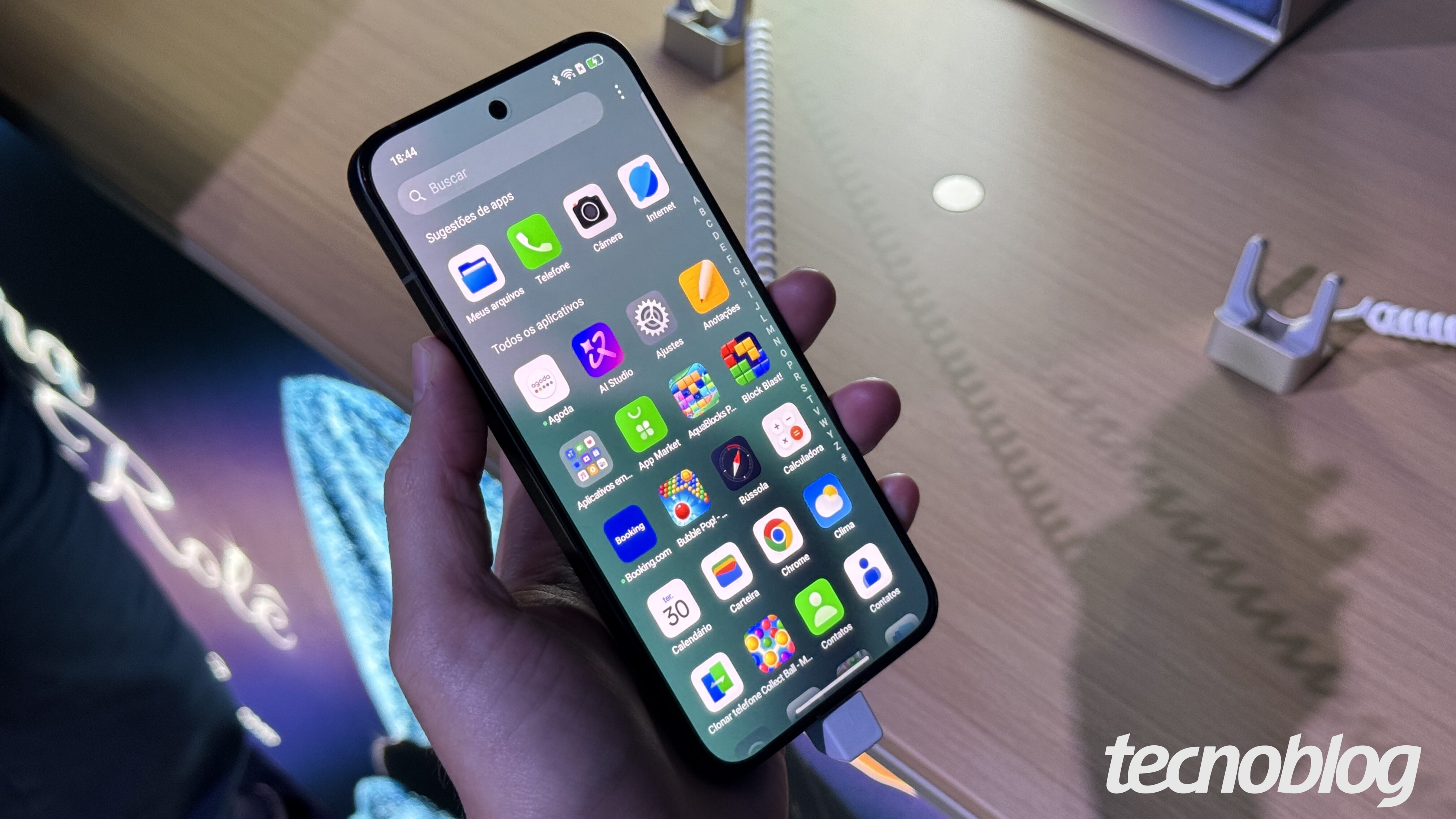 Foto mostra um celular Reno 14 da Oppo desbloqueado, sendo segurado em uma mão. Na parte inferior direita, a marca d'água do "tecnoblog".