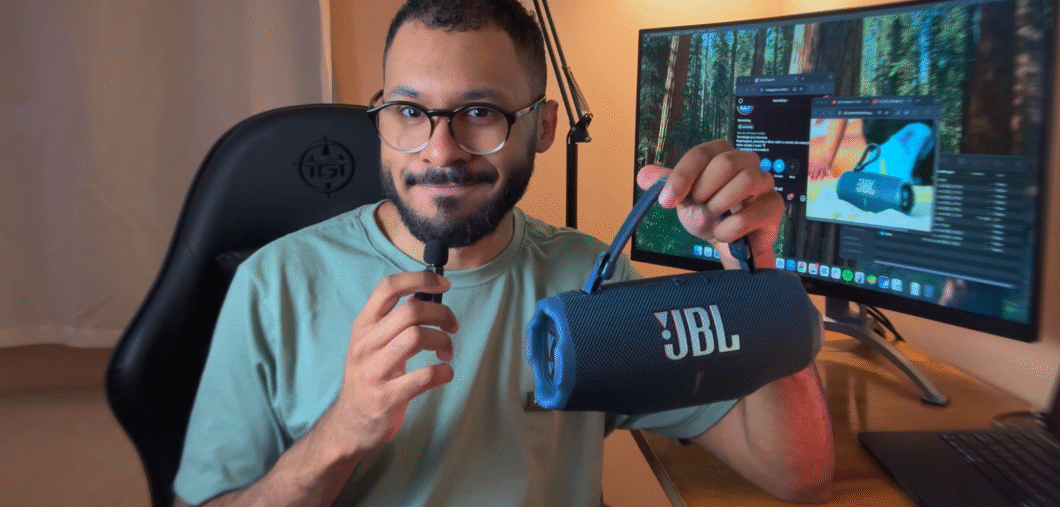 Homem sentado numa cadeira segurando a JBL Charge 6 pela nova alça. Ao fundo, um computador ligado.