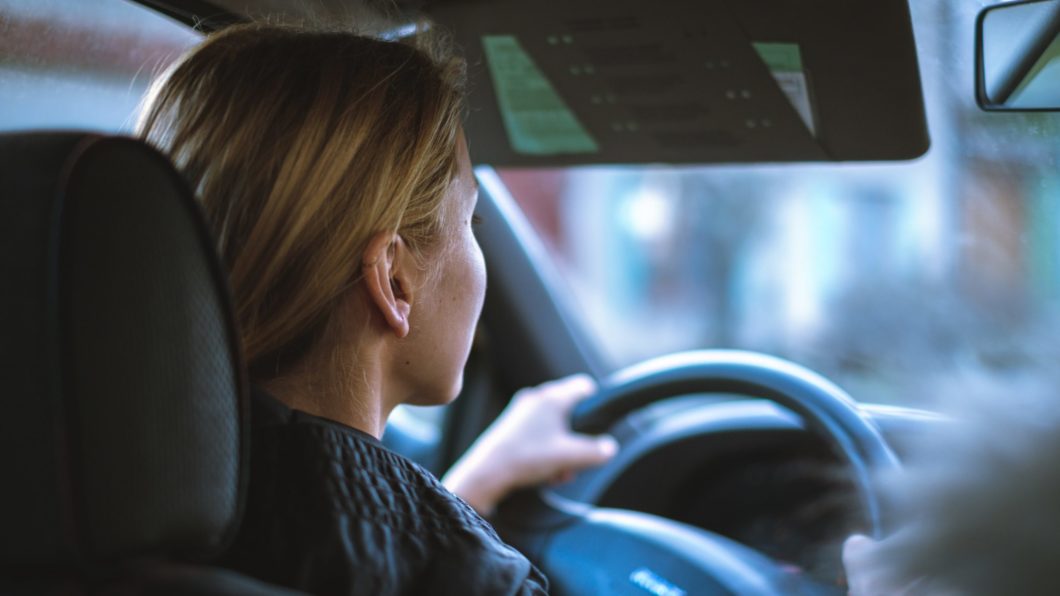 Imagem mostra uma mulher dirigindo um carro, com as mãos ao volante 