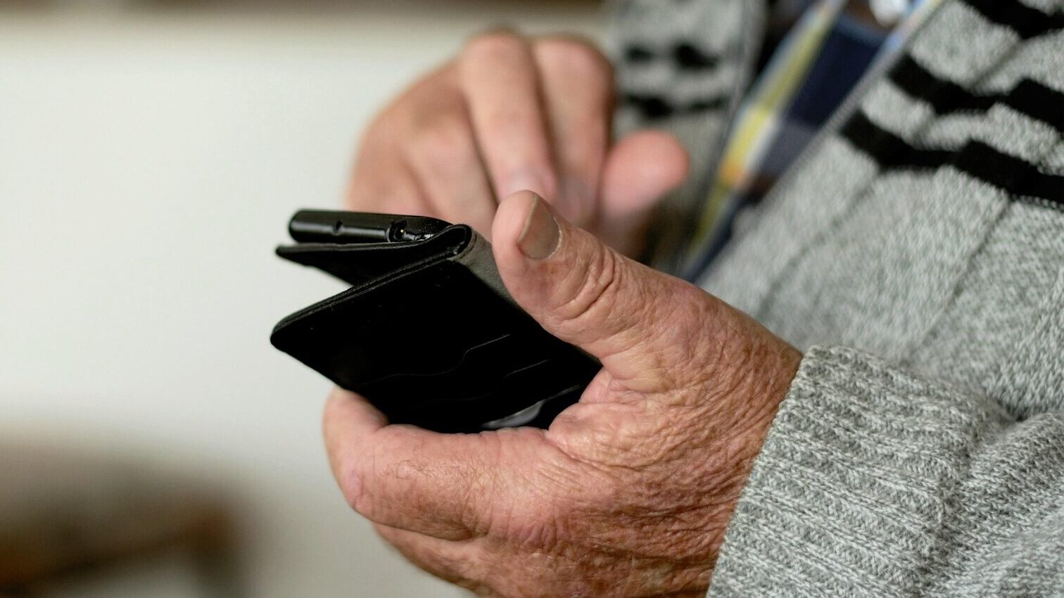 Foto de uma mão de uma pessoa idosa segurando um celular