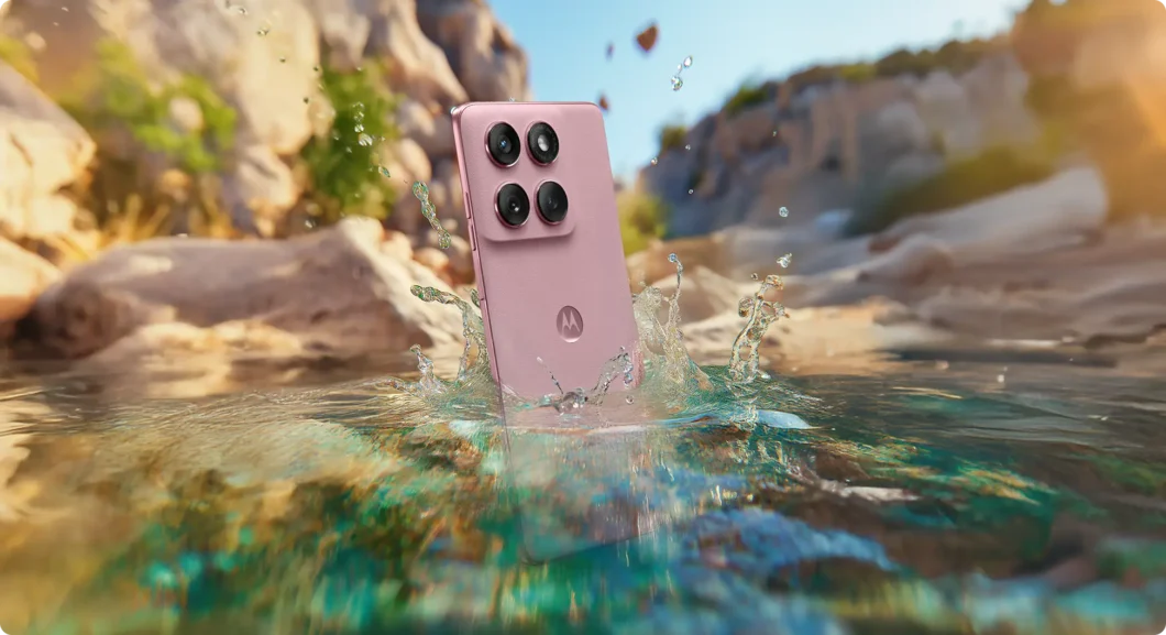 Smartphone Motorola Edge 60 Fusion na cor rosa caindo na água, destacando sua resistência à água, com um cenário de pedras e natureza ao fundo.