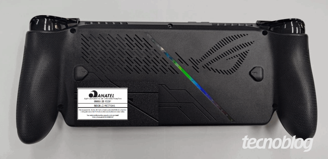 Imagem mostra a parte traseira de um console portátil ROG Xbox Ally X de cor preta, com a certificação da Anatel. Na parte inferior direita, o logo do "tecnoblog".