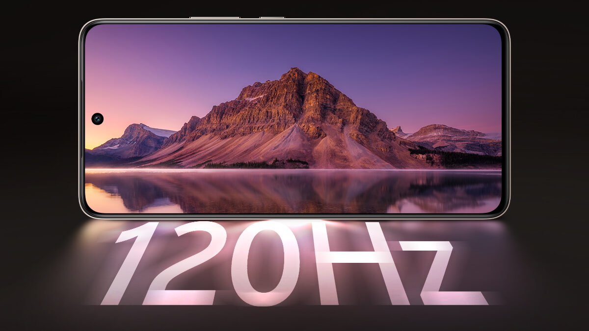Imagem de um smartphone em posição horizontal, com a tela exibindo uma fotografia de montanha refletida em um lago ao entardecer, em tons de roxo e dourado. O aparelho tem bordas finas e um pequeno recorte circular para a câmera frontal no canto superior esquerdo da tela. Abaixo do dispositivo, em letras grandes e iluminadas, aparece o texto “120Hz” projetado sobre o fundo preto.