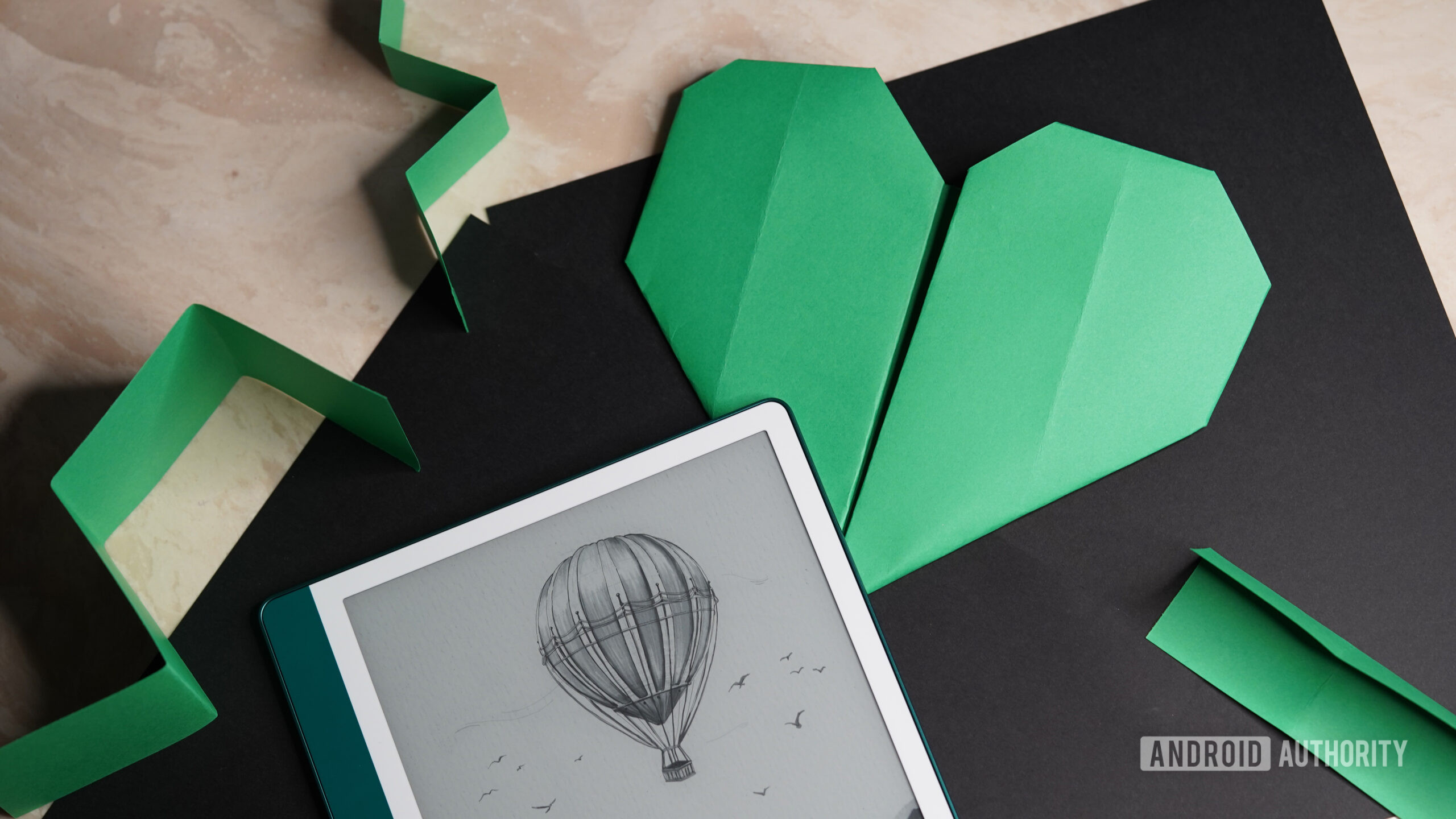 Um Kindle Scribe fica ao lado de um coração de origami.