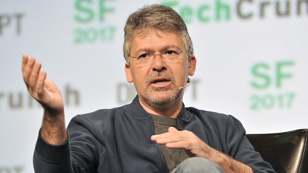 Imagem mostra um homem sentado durante uma apresenta&ccedil;&atilde;o. Ele usa &oacute;culos de grau e gesticula com as m&atilde;os 