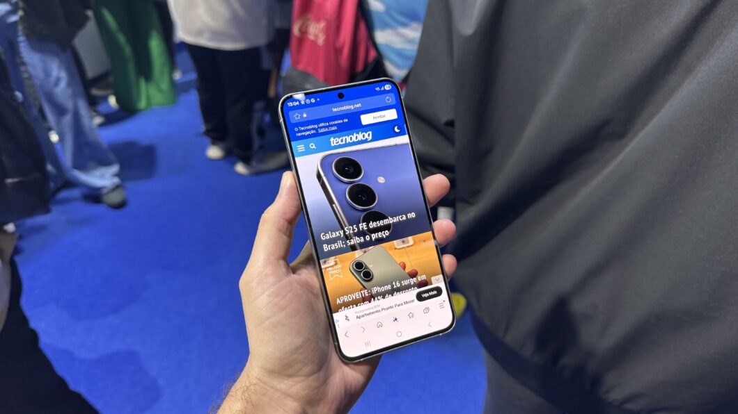 Galaxy S25 FE segurado por uma m&atilde;o com a tela pra cima e mostrando a home page do Tecnoblog.