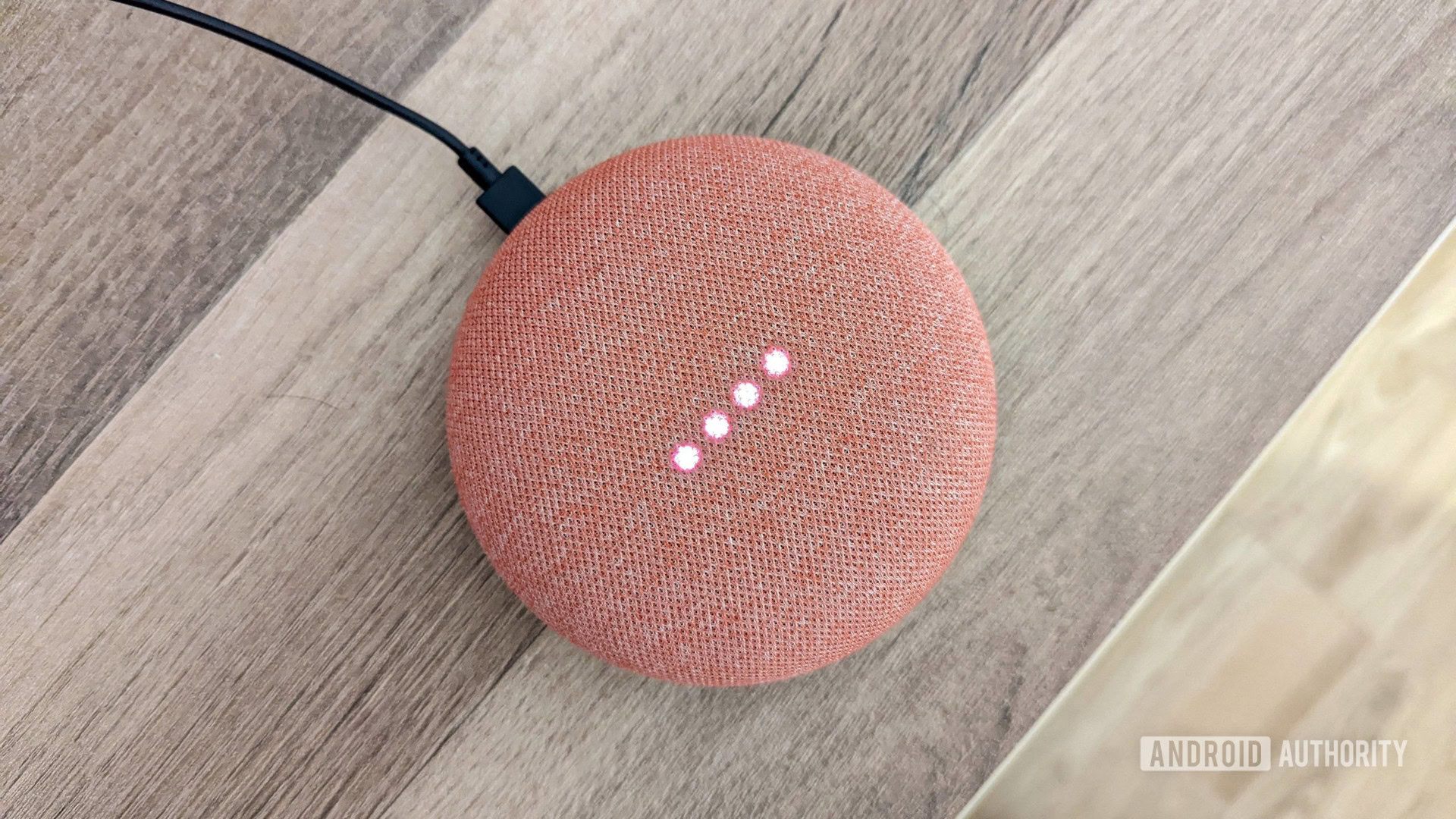 google home mini luzes coral acesas Google Home Mini em coral com luzes acesas, em fundo de madeira