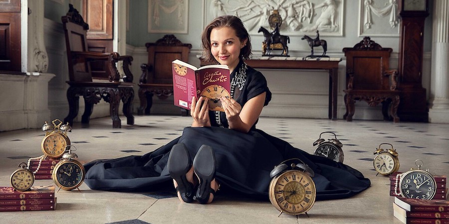 A woman sitting on the floor of an old house, surrounded by clocks