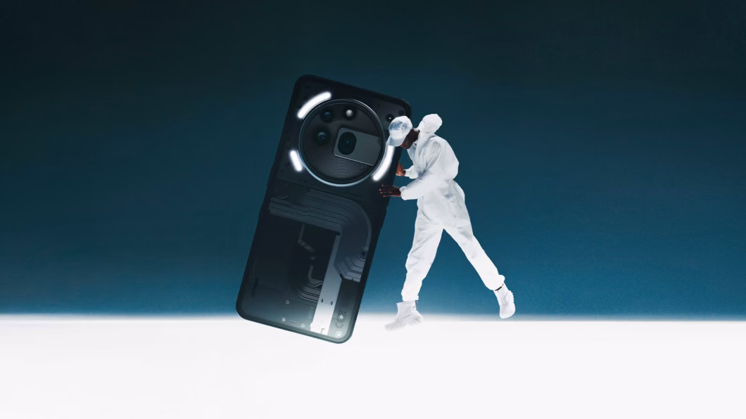 Imagem de um Nothing Phone 3a preto sendo segurado por um homem vestido completamente de branco. O fundo possui um degradê de preto ao azul escuro e uma borda inferior branca