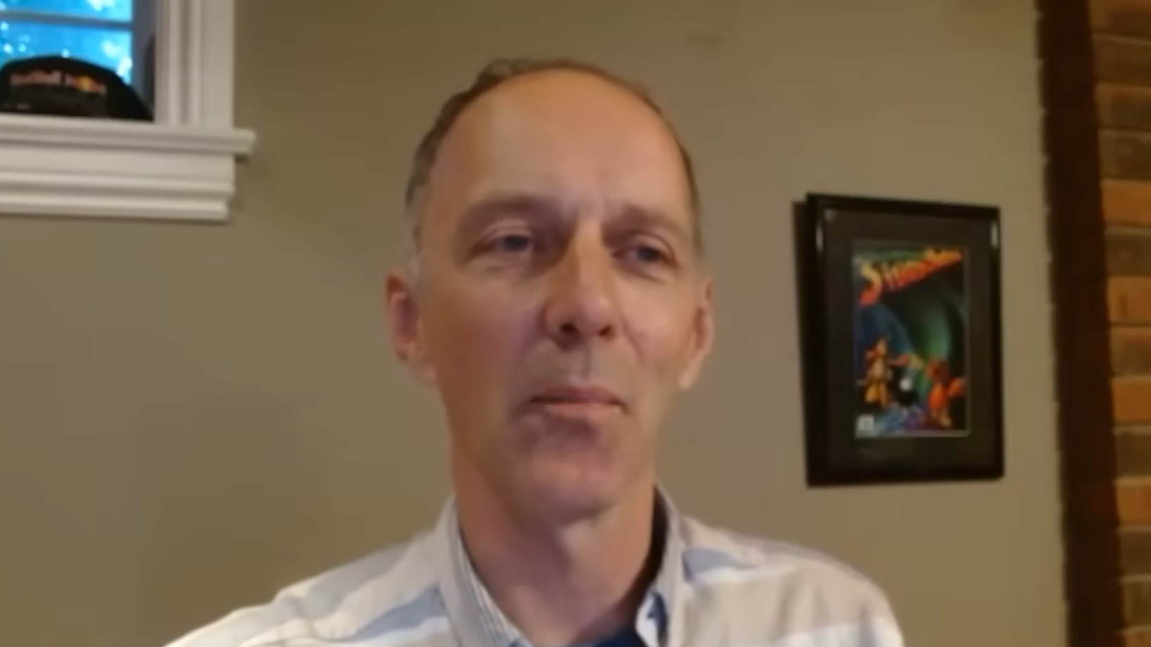 Imagem mostra um homem sentado, durante uma videochamada. No fundo, um quadro na parede.