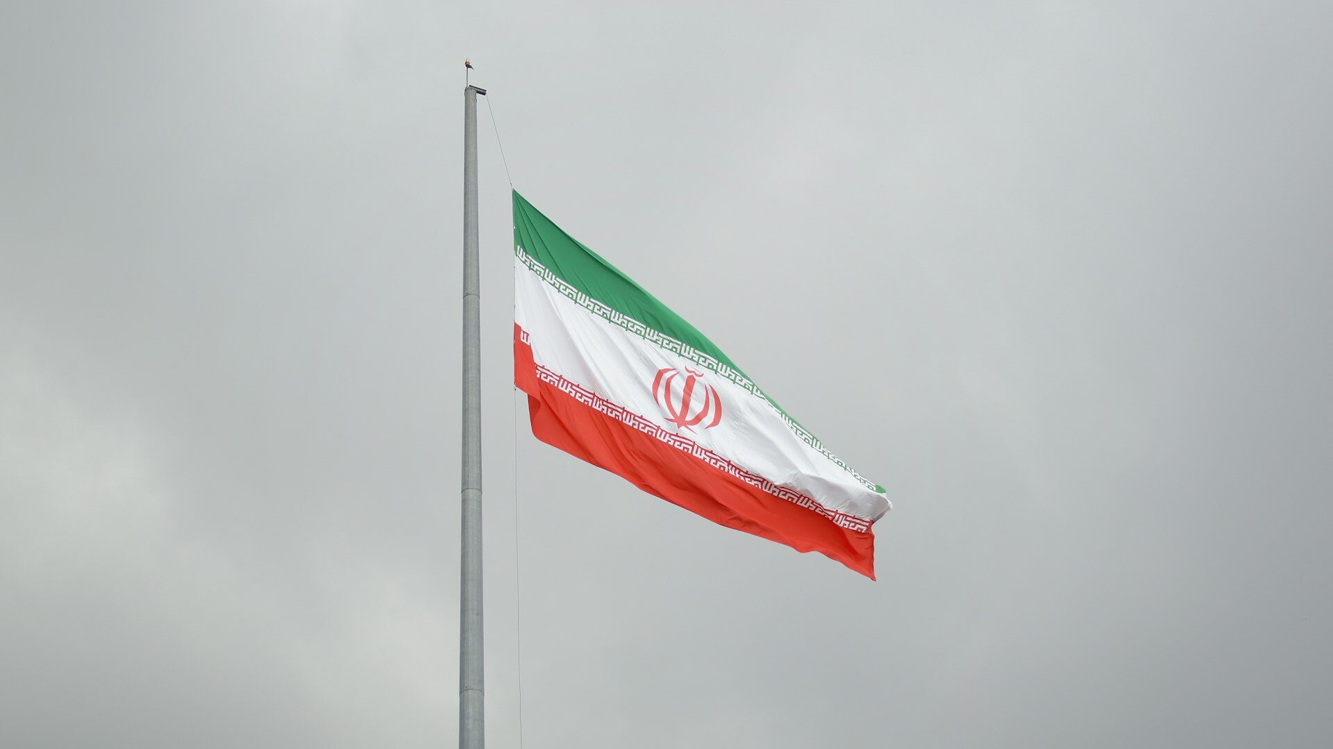 Bandeira do Ir&atilde; (verde, branca e vermelha, com um emblema isl&acirc;mico ao centro) hasteada em um dia nublado