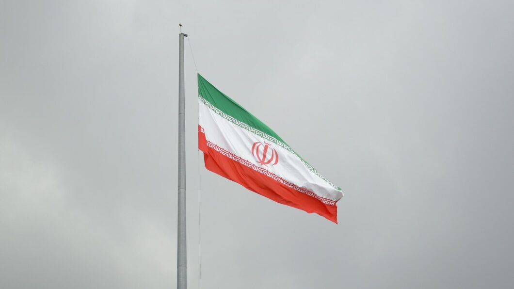 Bandeira do Ir&atilde; (verde, branca e vermelha, com um emblema isl&acirc;mico ao centro) hasteada em um dia nublado
