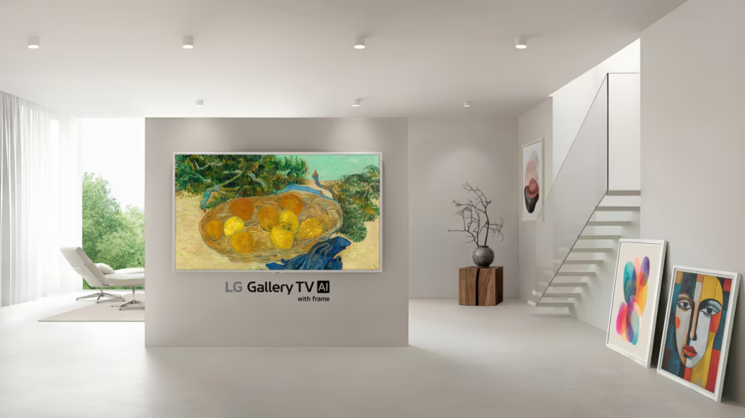 Sala moderna e minimalista, com uma TV da LG fixada na parede central como se fosse um quadro. Na tela, h&aacute; uma obra de arte colorida com frutas em uma cesta. Abaixo da TV, l&ecirc;-se &ldquo;LG Gallery TV AI&rdquo; e &ldquo;with frame&rdquo;. O ambiente tem escada &agrave; direita, quadros apoiados no ch&atilde;o e decora&ccedil;&atilde;o discreta, refor&ccedil;ando a ideia de galeria de arte.
