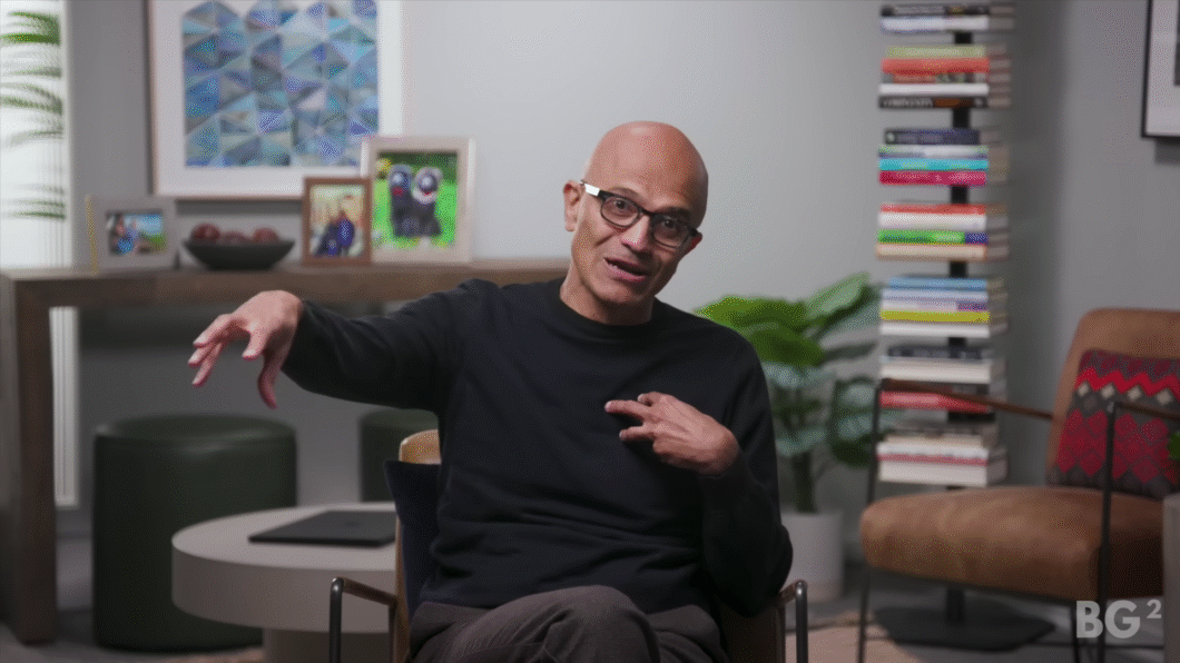 Homem calvo de &oacute;culos e su&eacute;ter preto gesticula com a m&atilde;o esquerda enquanto fala, sentado em uma cadeira em ambiente moderno e aconchegante, com livros empilhados verticalmente ao fundo, plantas e fotos emolduradas sobre uma mesa (imagem: reprodu&ccedil;&atilde;o/YouTube)