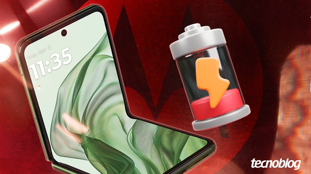 Imagem de um celular dobrável aberto exibindo a tela com data e hora, "Tue, Apr 3" e "11:35". Ao lado, há um ícone de bateria com nível baixo, representado por um cilindro parcialmente vermelho e um raio laranja sobre ele. O fundo é vermelho com um padrão sutil e o logo da Motorola em tons escuros. No canto inferior direito está a marca d’água "Tecnoblog".