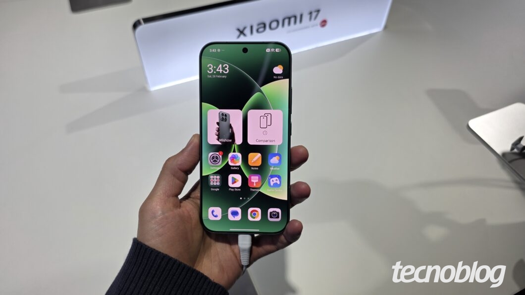 M&atilde;o segurando Xiaomi 17 com tela acesa, exibindo &iacute;cones de aplicativos na interface HarmonyOS 3