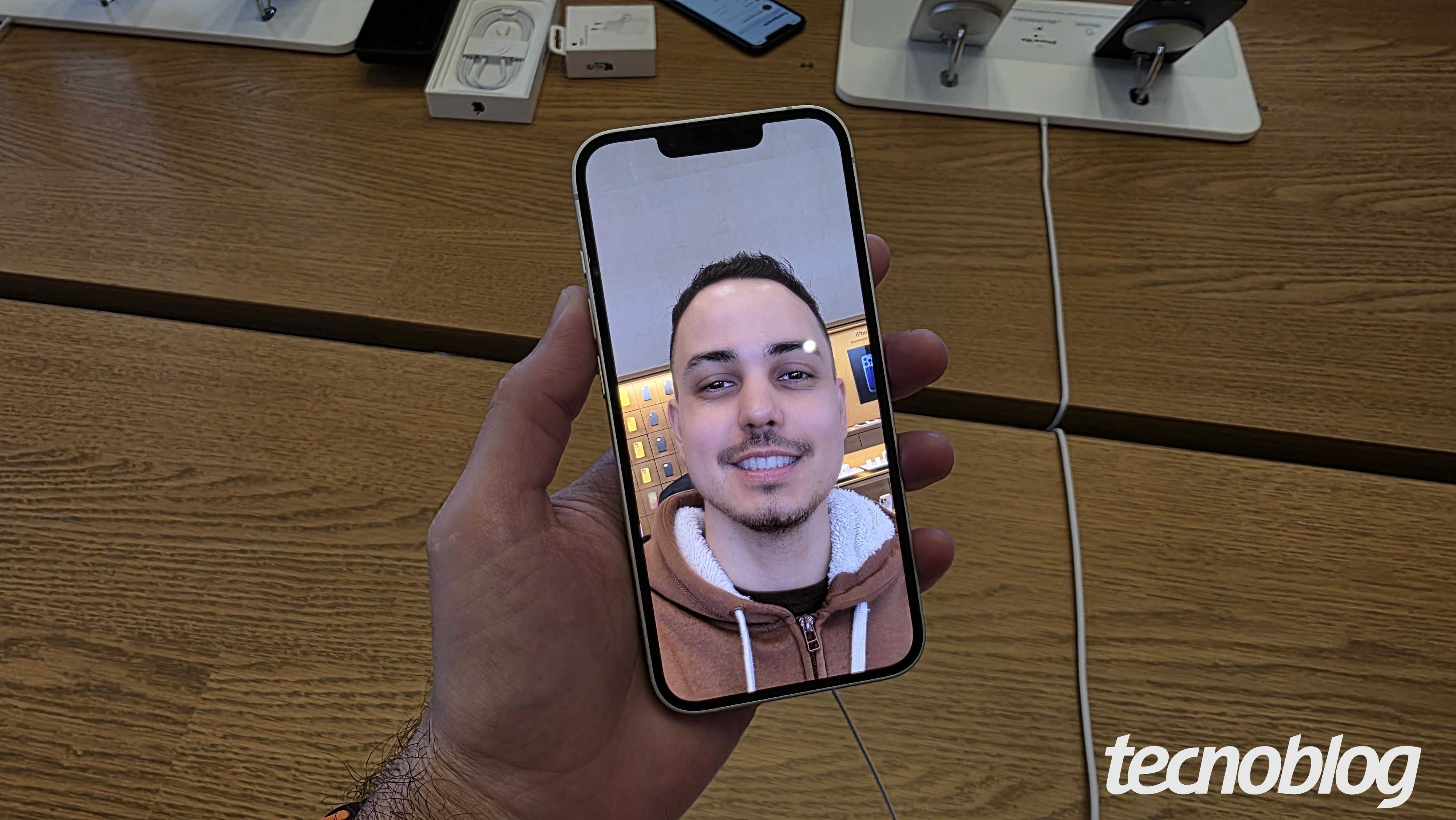 Fotografia colorida mostra um iPhone 16e sendo segurado em uma m&atilde;o. Ele est&aacute; com a c&acirc;mera frontal aberta.