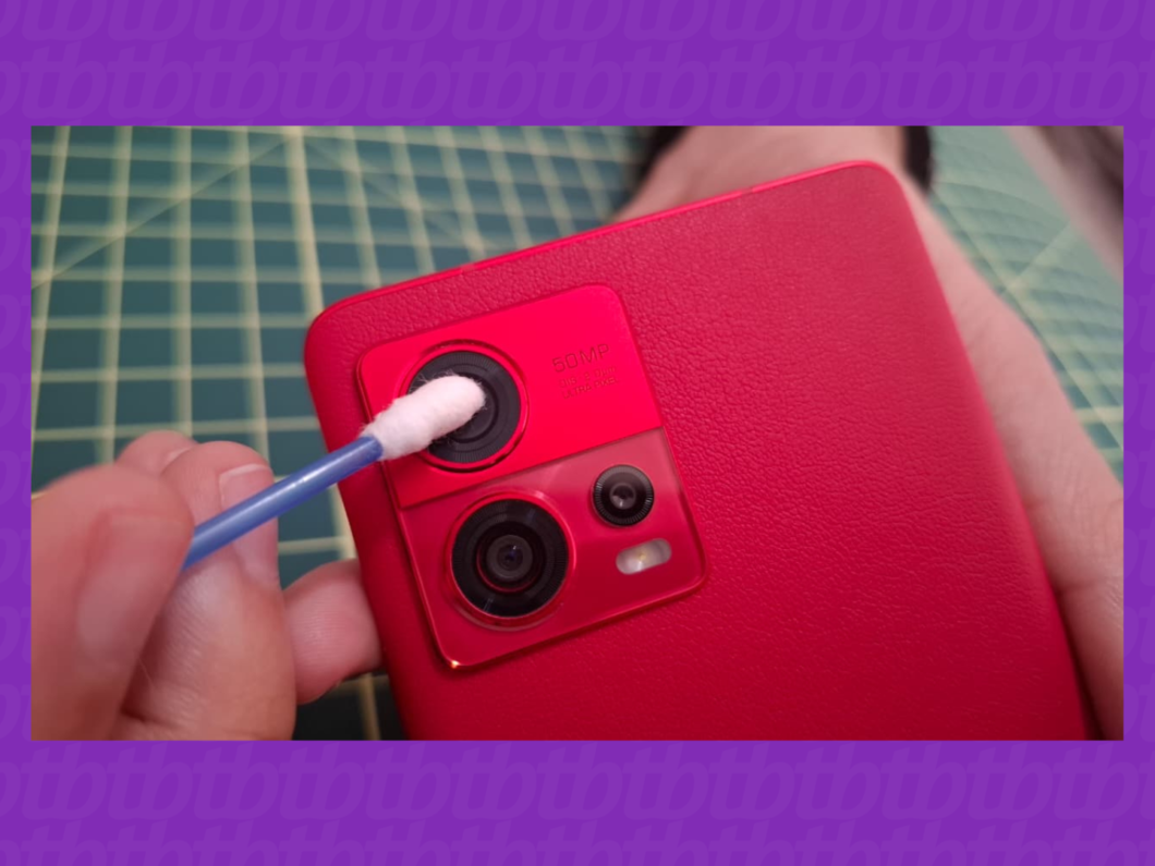 imagem de uma mão limpando a lente da câmera de um celular com cotonete