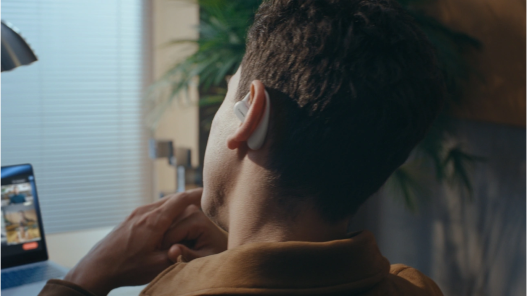 Homem sentado olhando para um computador sobre a mesa com o Huawei FreeArc na orelha