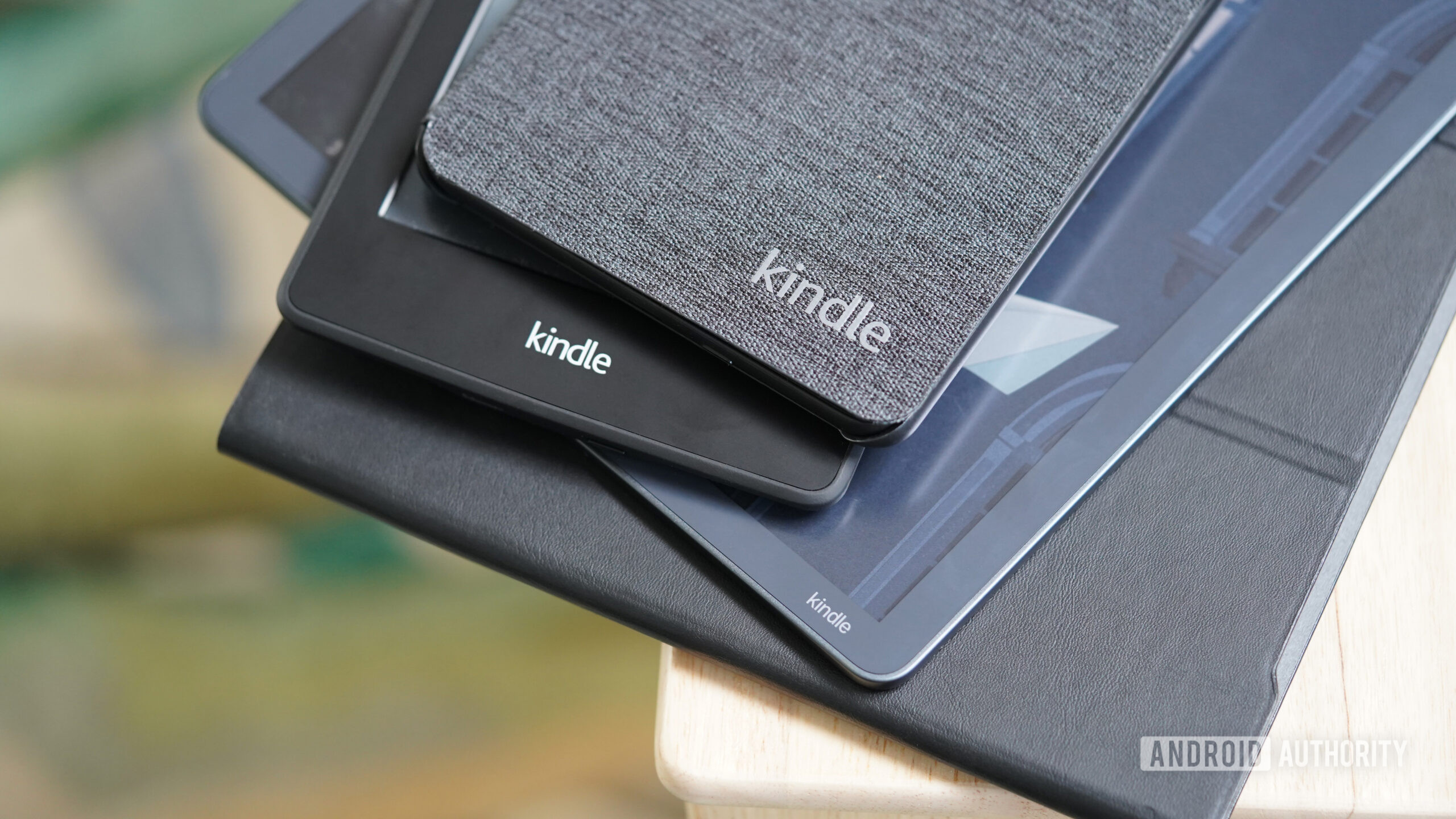 Pilha Amazon Kindle variada Uma pilha de Kindles da Amazon está sobre uma mesa de cabeceira.