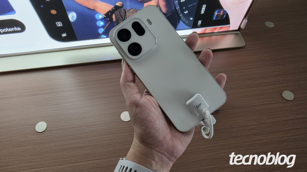 M&atilde;o segurando Oppo Find X9 Pro na cor branca sobre mesa de madeira