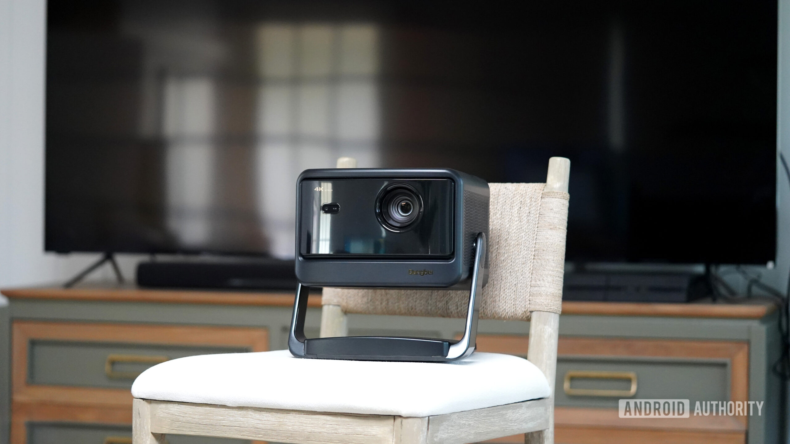 Um projetor port&aacute;til fica em frente a uma TV moderna.