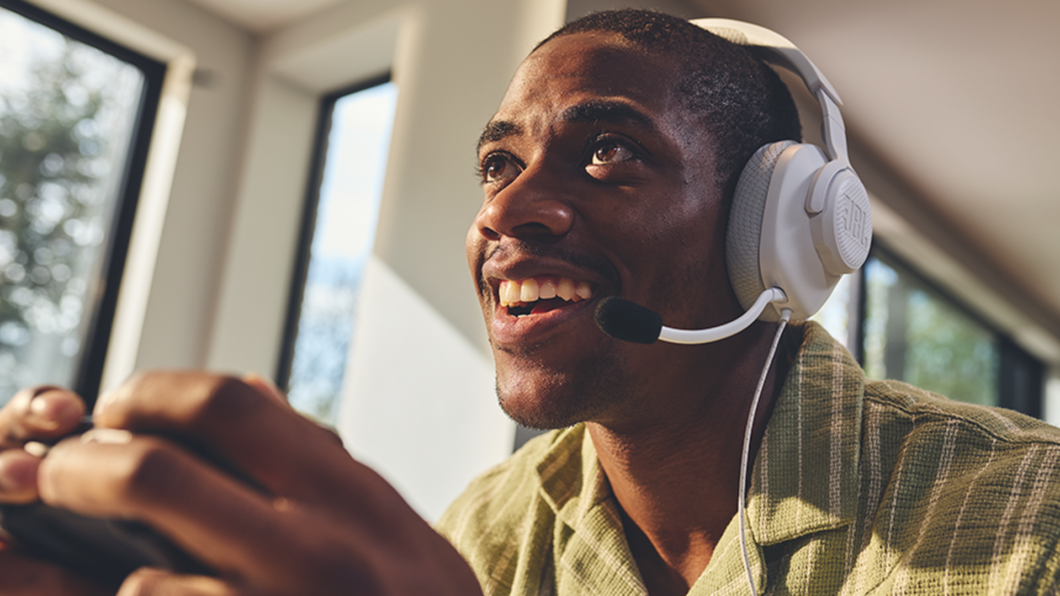 Homem utilizando o JBL Quantum 100M2 na cor branca e segurando um controle de videogame nas m&atilde;os.
