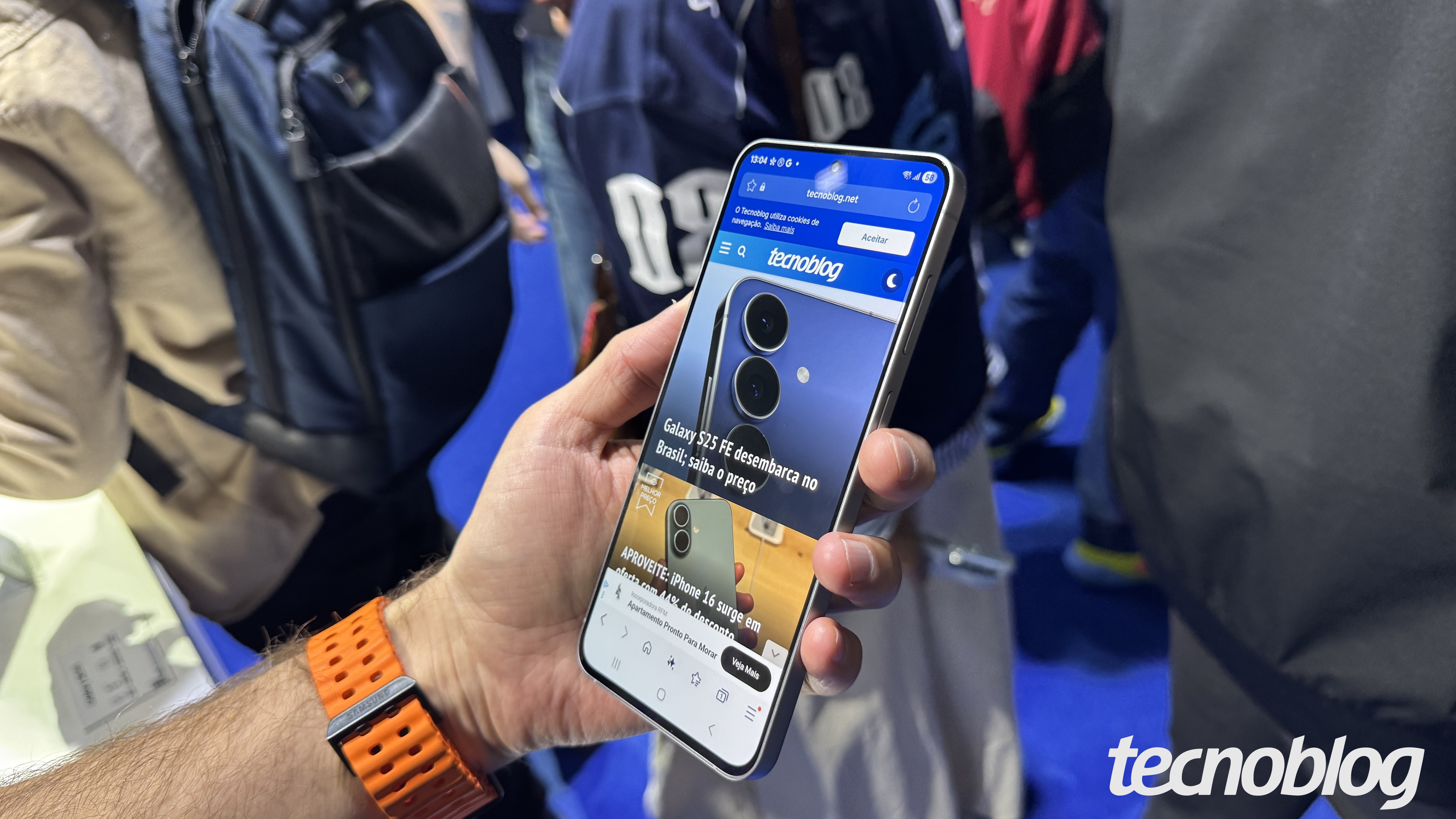 Galaxy S25 FE segurado por uma mão com a tela pra cima e mostrando a home page do Tecnoblog.
