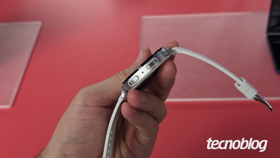 Mão segurando smartwatch com tela desligada, visto de lado, mostrando os botões