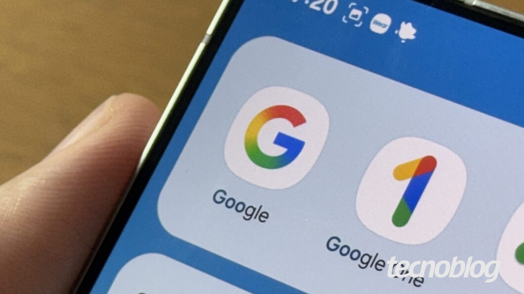 A imagem mostra a tela de um smartphone sendo segurado por uma m&atilde;o. Na parte superior da tela, &eacute; poss&iacute;vel ver a hora "17:20" e &iacute;cones de notifica&ccedil;&atilde;o. Abaixo, h&aacute; tr&ecirc;s &iacute;cones de aplicativos: o logo colorido do Google, o &iacute;cone do Google One e o &iacute;cone do Google Ads, todos com design simples e minimalista. A interface do sistema est&aacute; em um fundo azul claro. A m&atilde;o que segura o dispositivo est&aacute; posicionada na lateral.