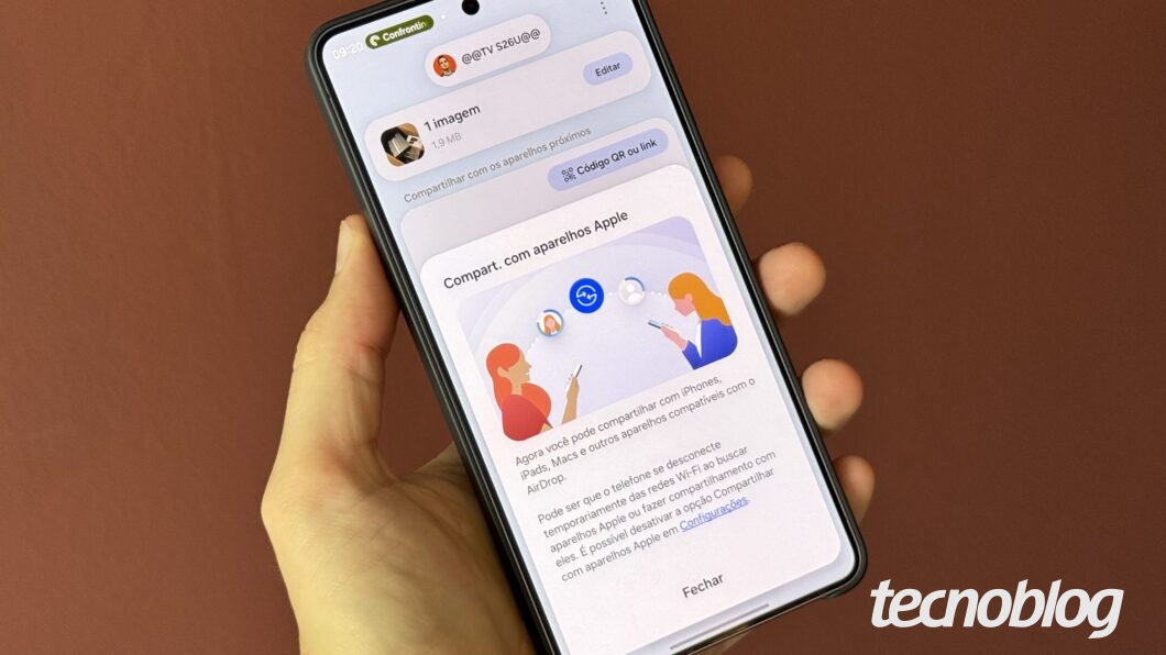 M&atilde;o segurando celular, com aviso de compartilhamento na tela
