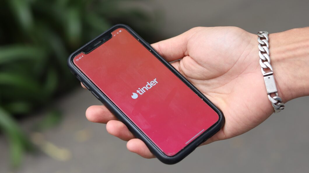 Imagem mostra uma m&atilde;o segurando um iPhone, com a tela exibindo o logo do Tinder