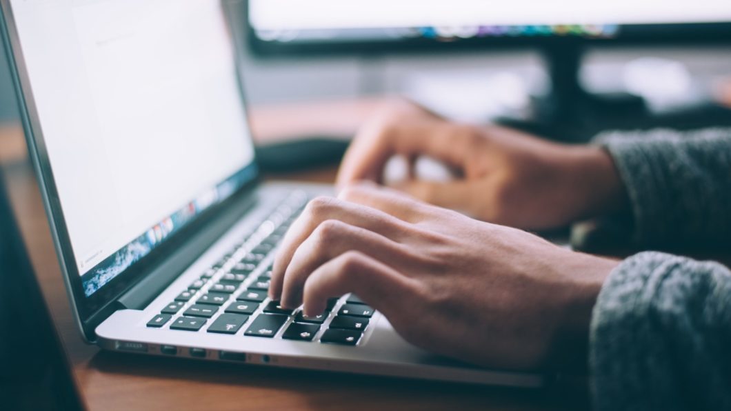 Imagem mostra duas mãos digitando em um MacBook
