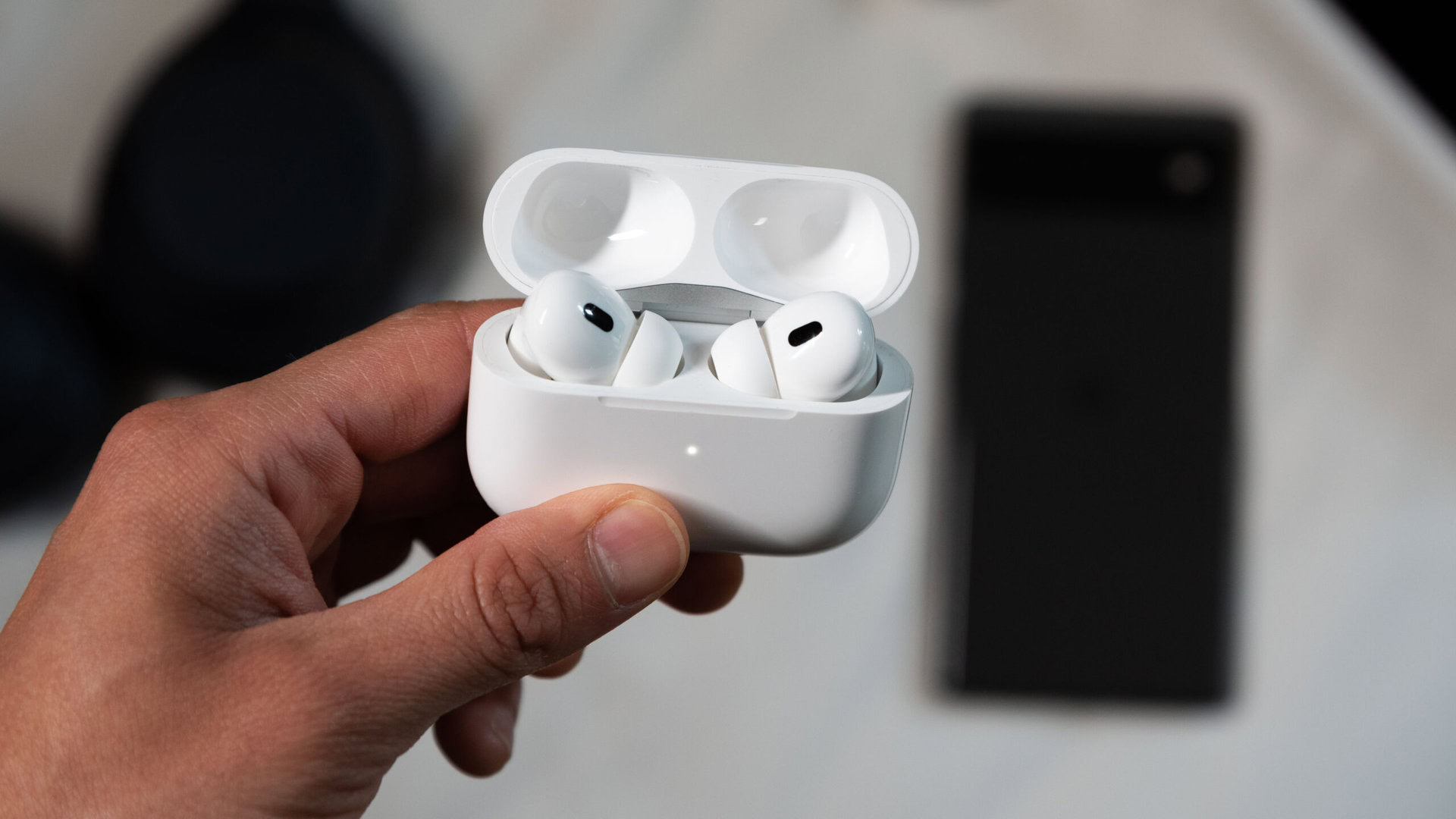 Uma mão segura o AirPods Pro de 2ª geração no modo de pareamento na frente de um smartphone Pixel 6.