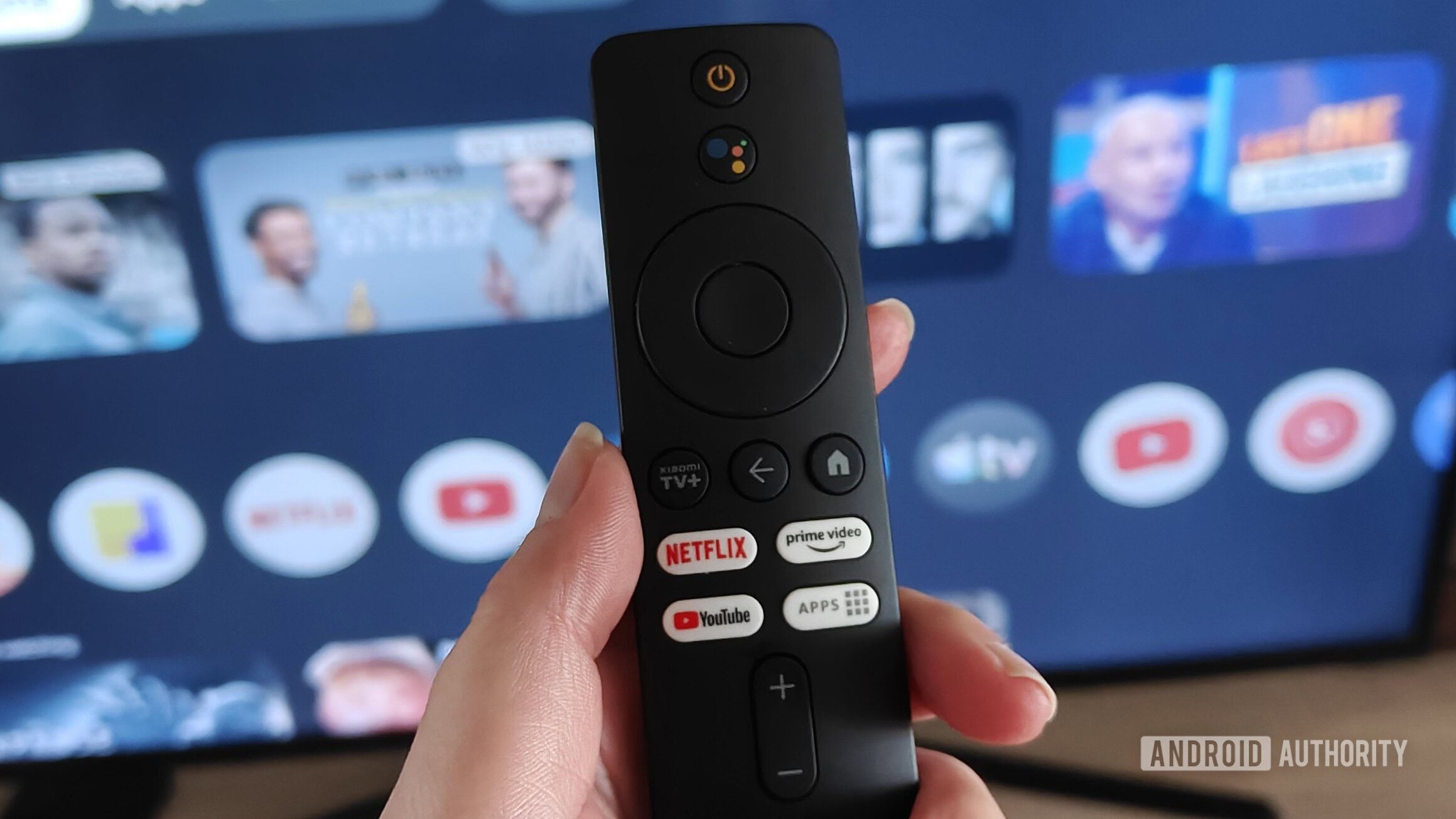 um controle remoto segurado na mão com a interface do Google TV em uma tela ao fundo