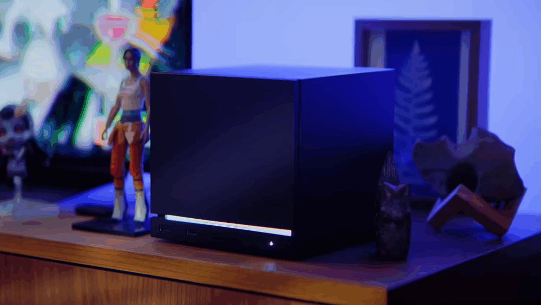 Imagem exibe uma Steam Machine sobre uma mesa de madeira. Se trata de um cubo preto, com um led branco na parte inferior.